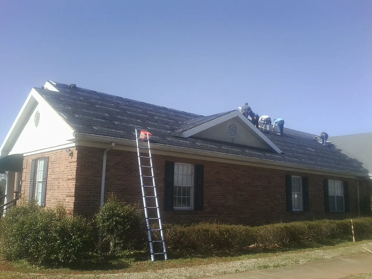 Crew tearing shingles off a brick ranch roof with a ladder set — Metal Roof Repair work by our crew in Julian