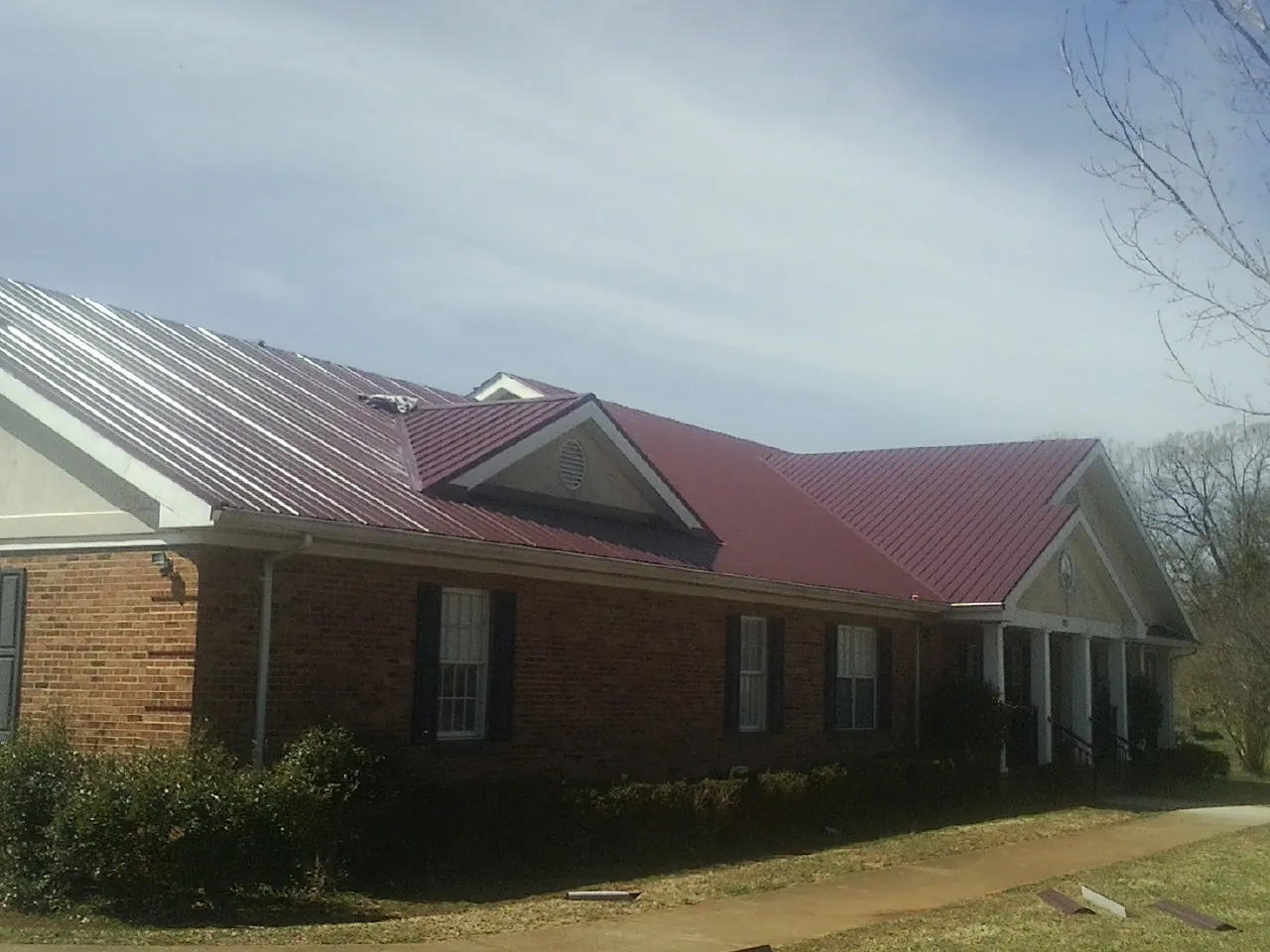 Red metal roof with gabled entries on a long brick building, from a Hail Damage Roof Repair job in Julian