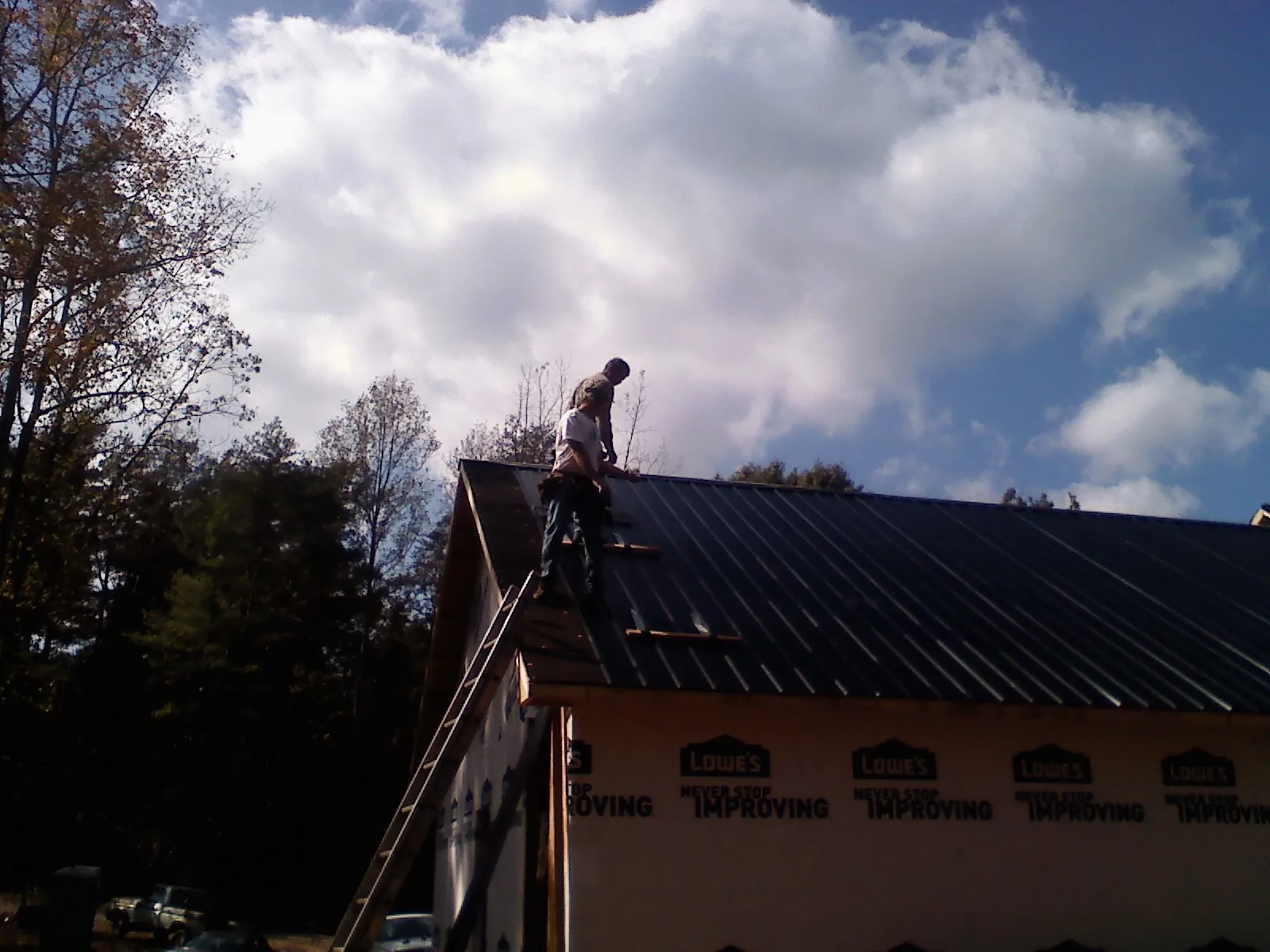 Roofer fastening dark metal panels high against a cloudy sky, from a Roof Inspection job in Julian